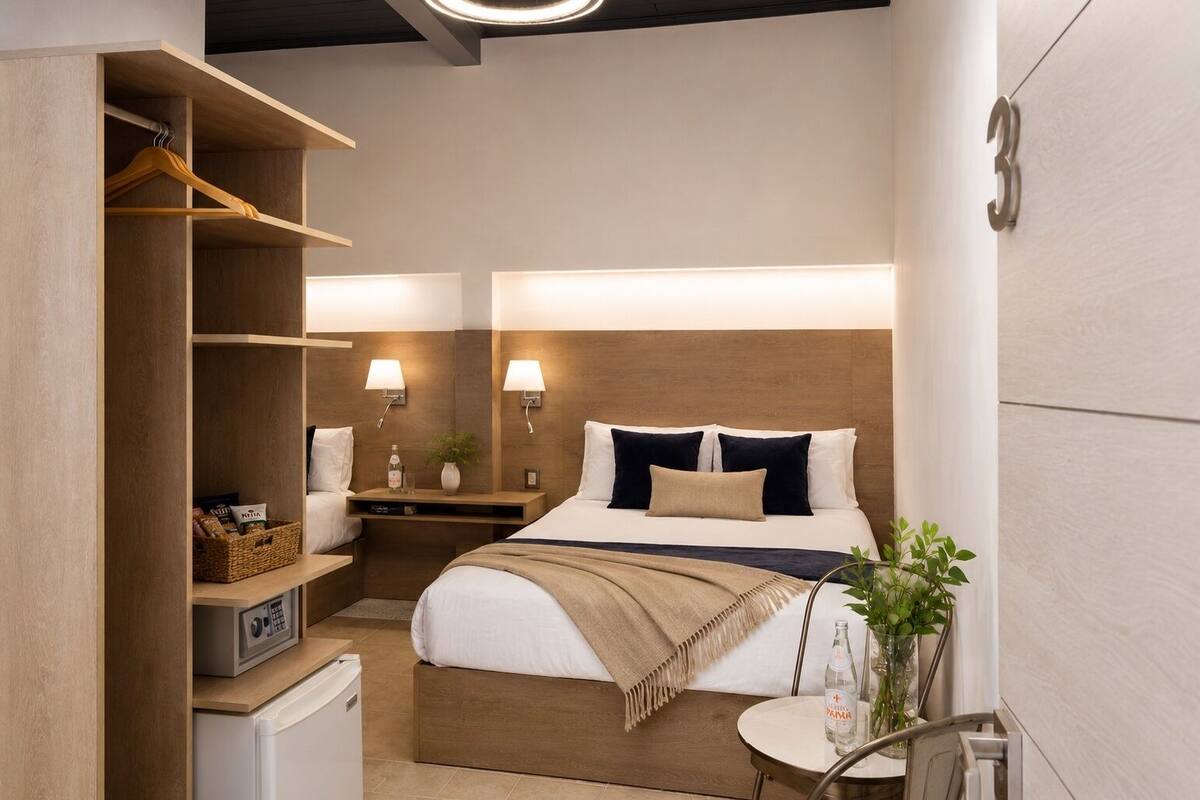 A hotel room with a bed, bedside tables, a wardrobe, a small desk, a microwave, and a round table with a plant.