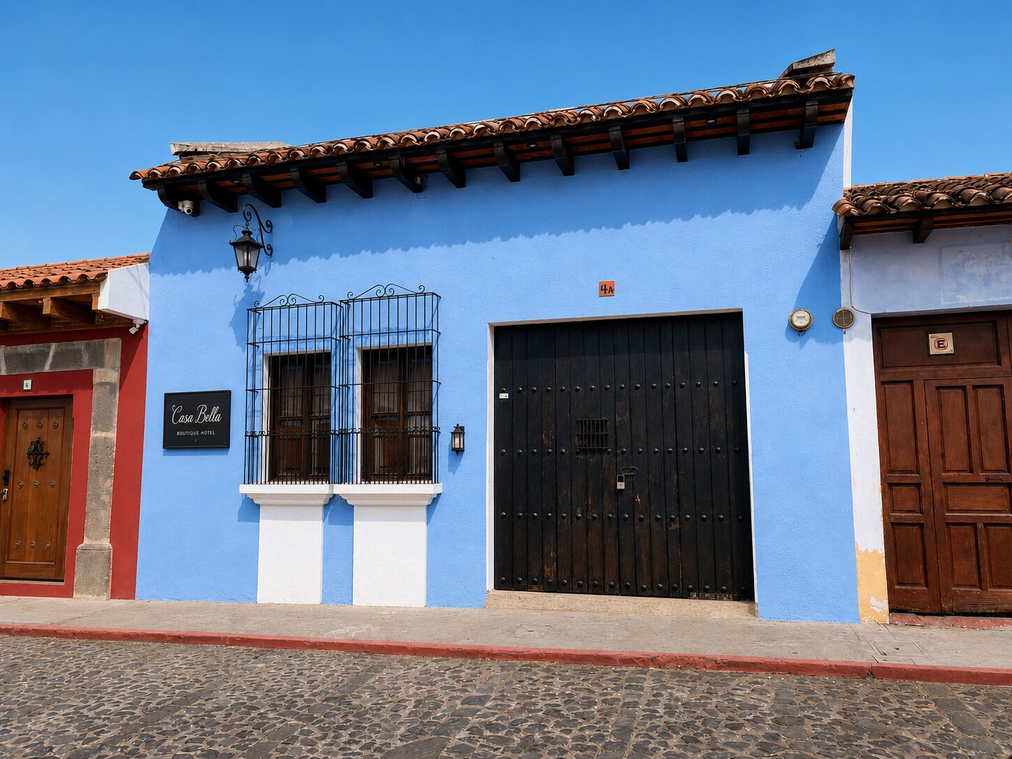 Een blauw gebouw met een zwarte deur, een raam met metalen tralies en een bord waarop staat 'Casa Bella Boutique Hotel'.