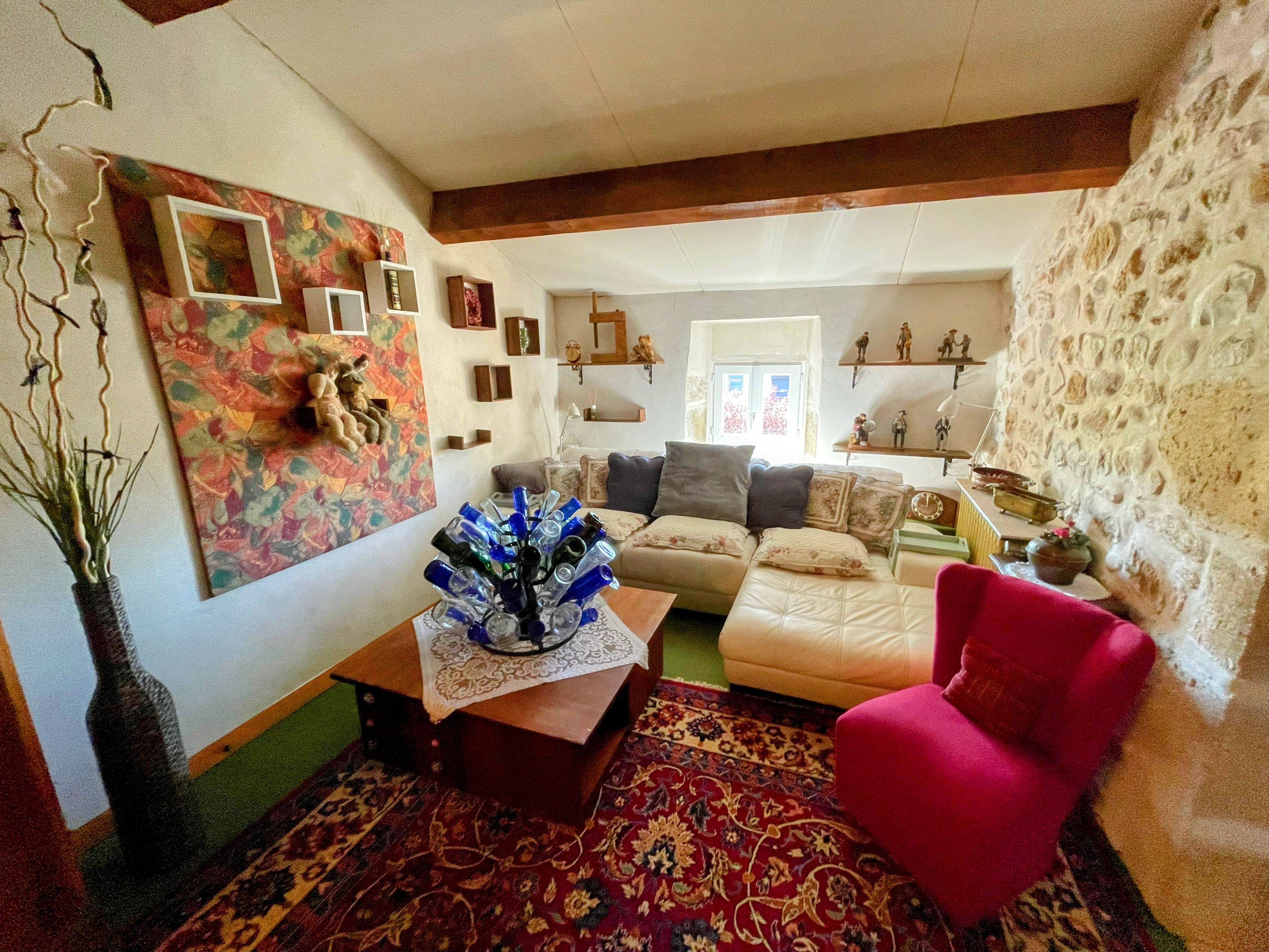 A living room with a sofa, a red armchair, a coffee table with a vase, and a patterned rug.