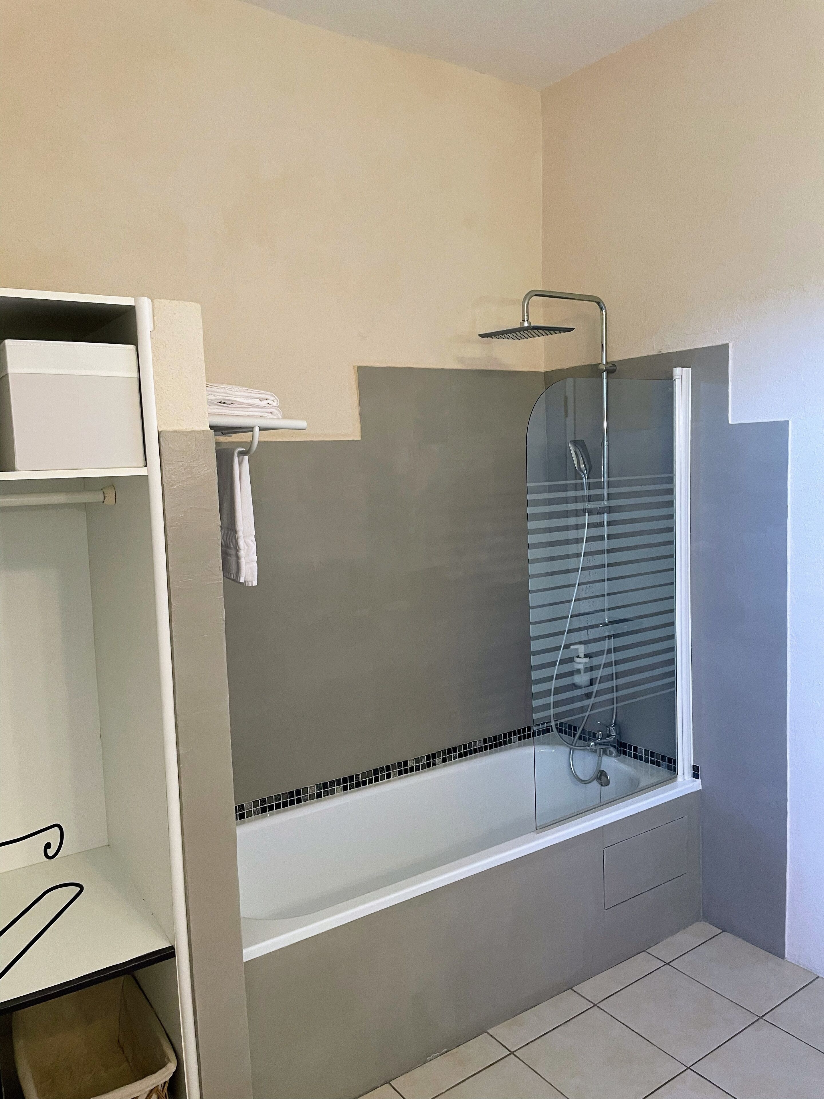 Une salle de bain moderne avec une douche à parois de verre, une baignoire blanche et une étagère sur laquelle est posée une serviette.