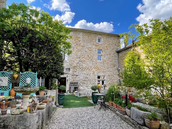 A stone building with a courtyard, surrounded by potted plants and outdoor furniture. - Hotel le Manoir du Raveyron (Vallon-Pont-d'Arc)