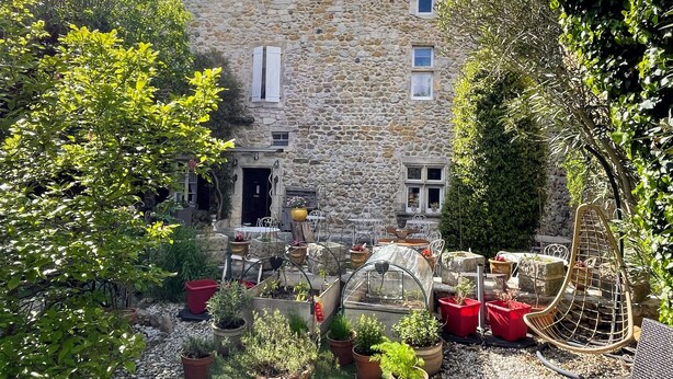 Un edificio in pietra con un giardino antistante, che include piante in vaso e una serra.