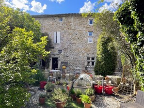 A stone building with a garden in front, including potted plants and a greenhouse. - Hotel le Manoir du Raveyron (Vallon-Pont-d'Arc)