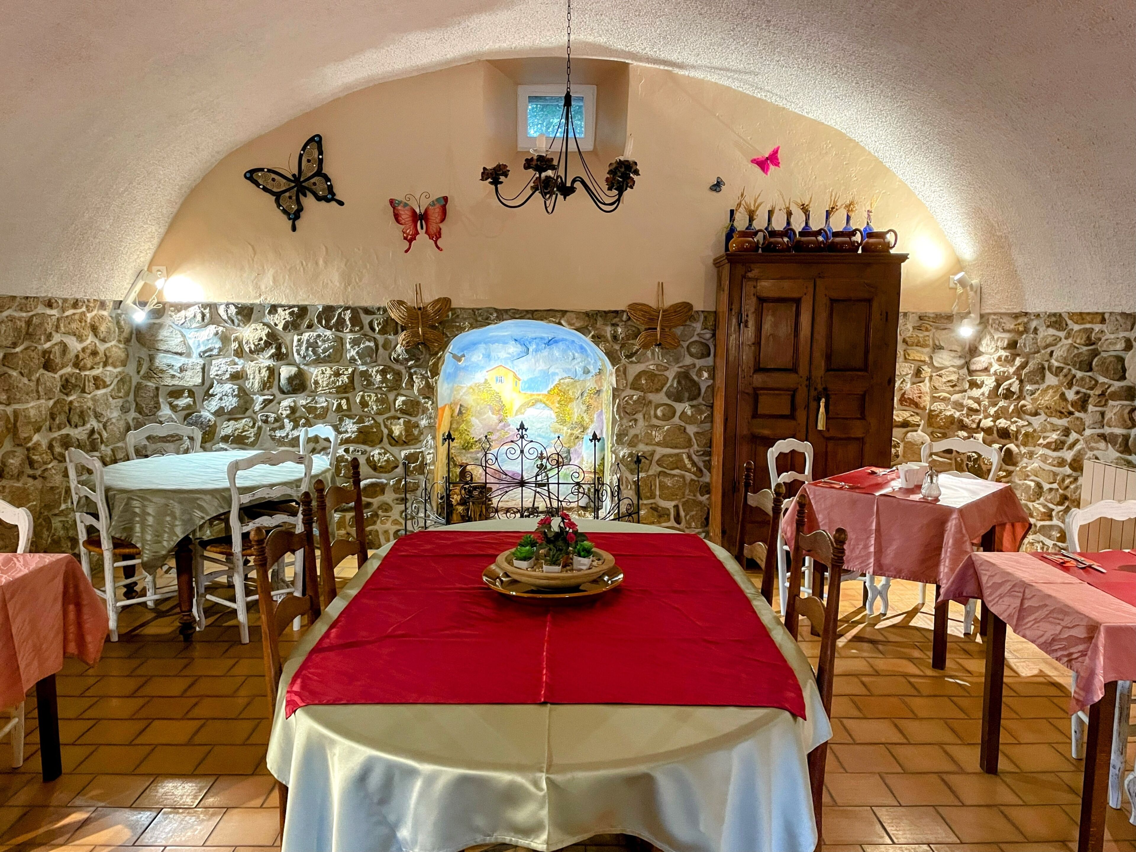 Un espace repas avec des murs en pierre, une fresque murale et une nappe rouge.
