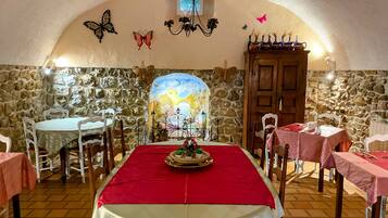 Un espace repas avec des murs en pierre, une fresque murale et une nappe rouge.