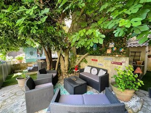 A patio area with wicker furniture, a potted plant, and a stone wall with signs. - Hotel le Manoir du Raveyron (Vallon-Pont-d'Arc)