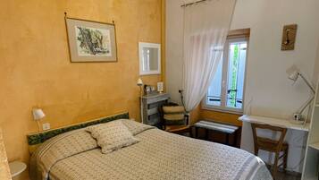A bedroom with a bed, a desk, a chair, a window with curtains, a chandelier, and a wall with a pattern.