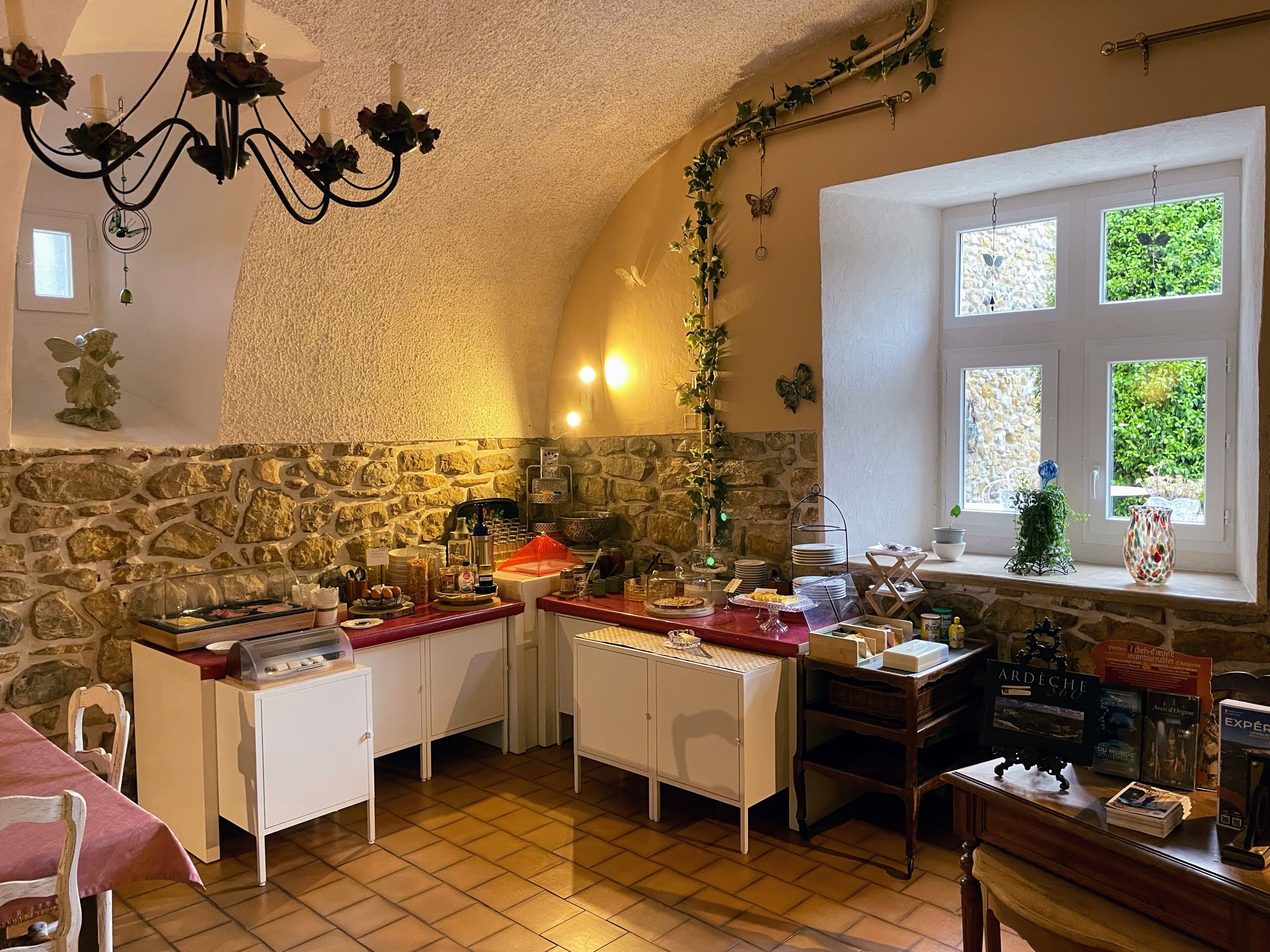 A cozy kitchen with stone walls, a chandelier, and a window with a view.