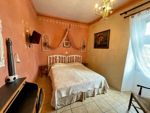A bedroom with a bed, a wooden nightstand, a lamp, and a window with curtains. - Hotel le Manoir du Raveyron (Vallon-Pont-d'Arc)