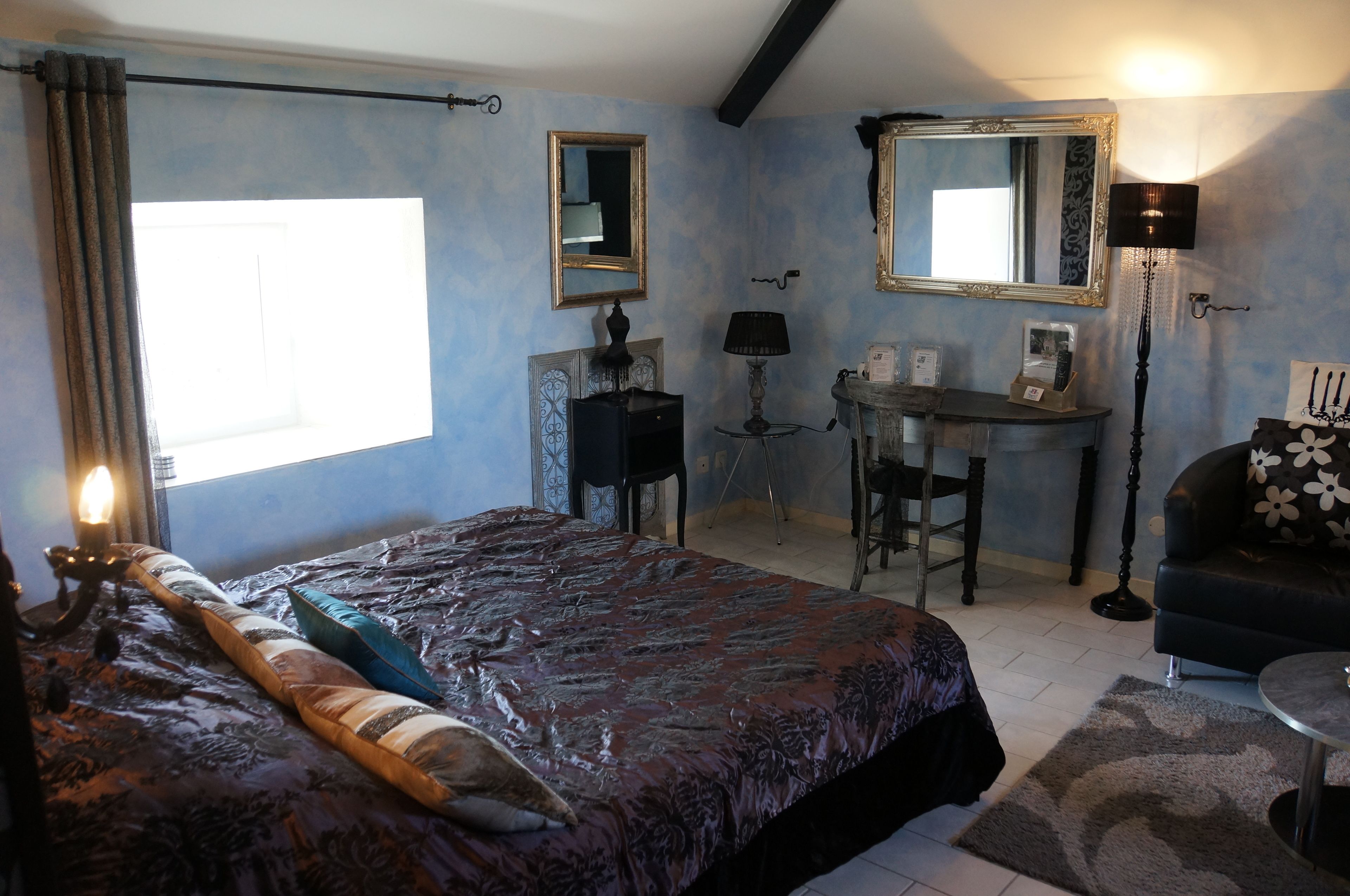 Ein Schlafzimmer mit einem Bett, einem Schreibtisch, einem Sessel, einer Couch und einem Spiegel.
