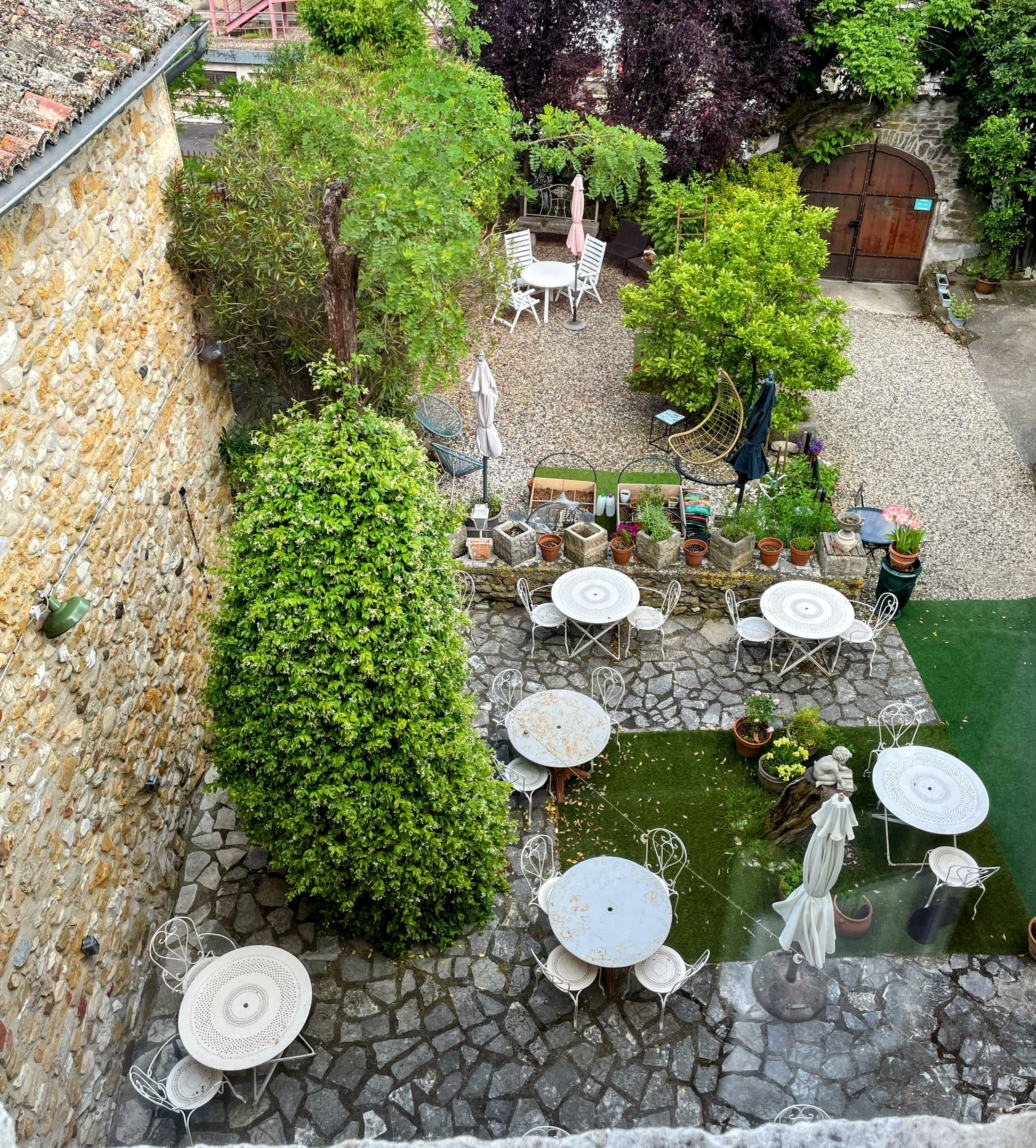 Un mur de pierre bordé d’un petit jardin agrémenté d’une table et de chaises en pierre, le tout entouré de verdure et d’un petit étang.