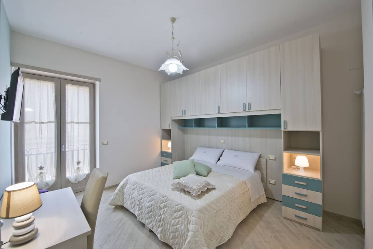 Um quarto com cama, mesas de cabeceira, escrivaninha e guarda-roupa.