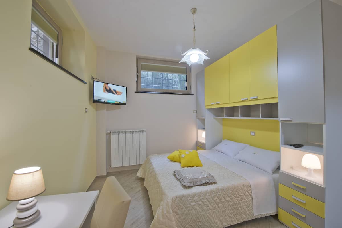 Quarto com cama, televisão, luminária e janela.