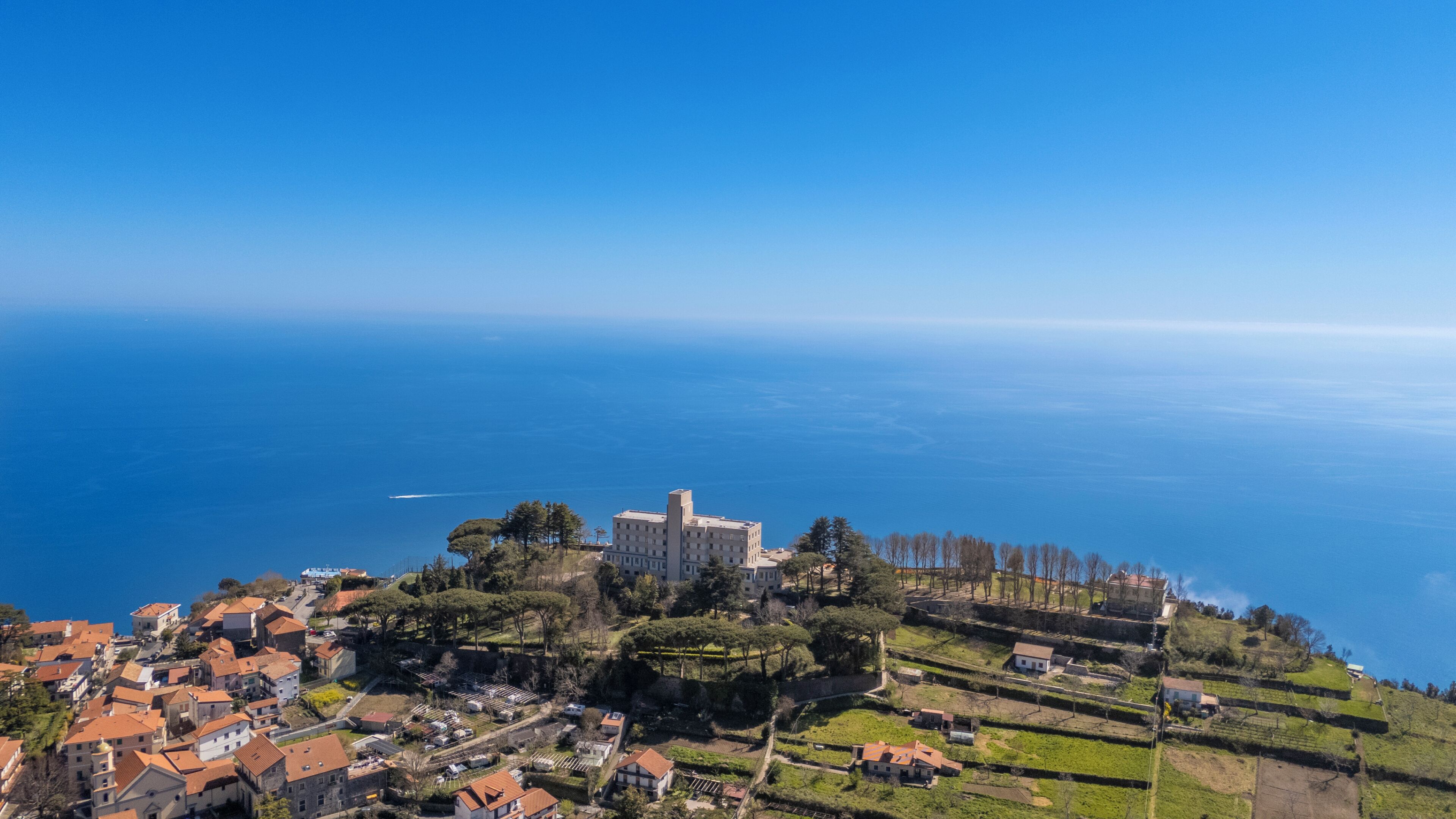 Un poble costaner amb un edifici destacat, terrasses agrícoles i una vista clara del mar.