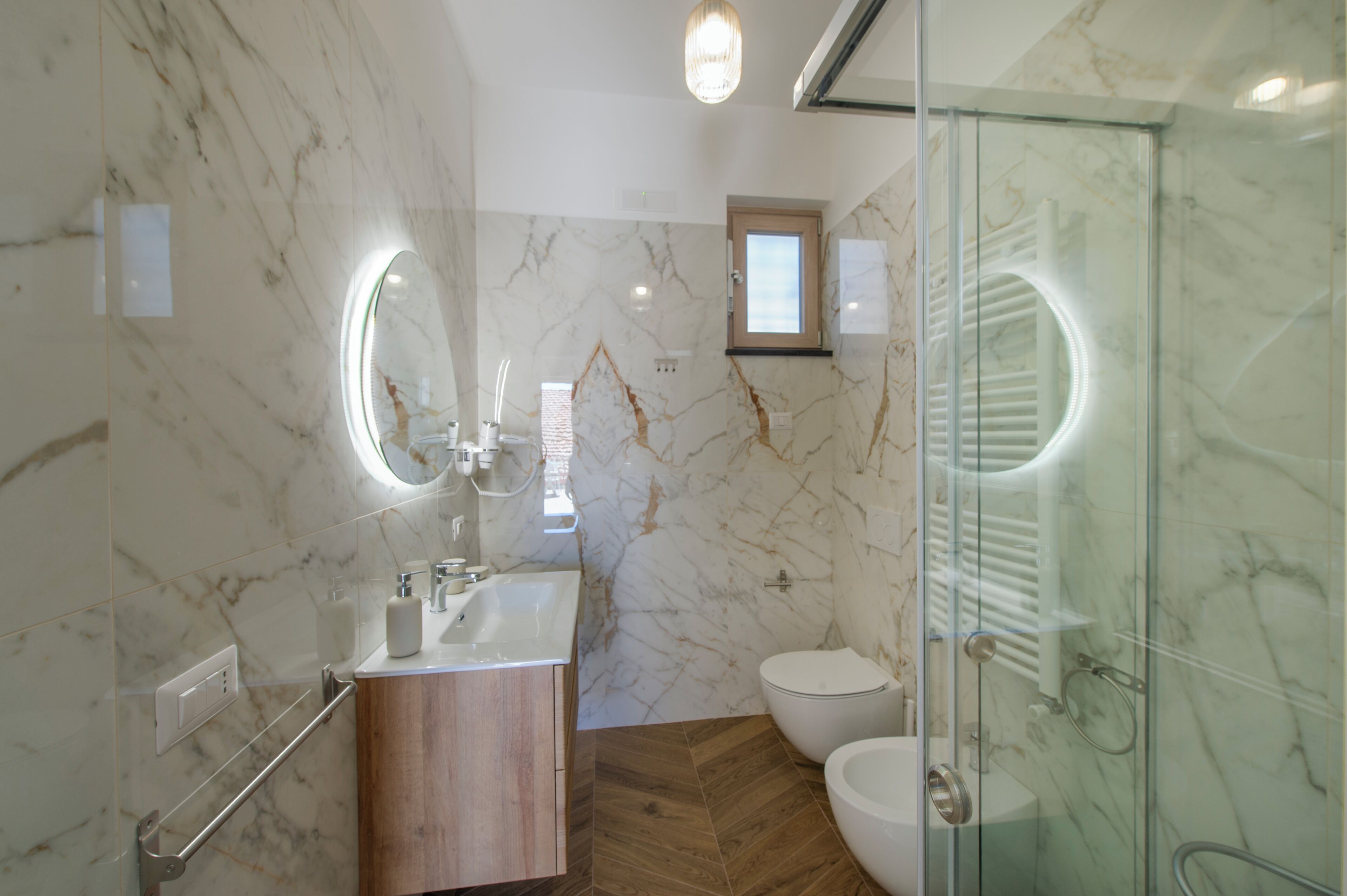 A modern bathroom with a marble wall, a wooden vanity, a glass shower enclosure, and a toilet.