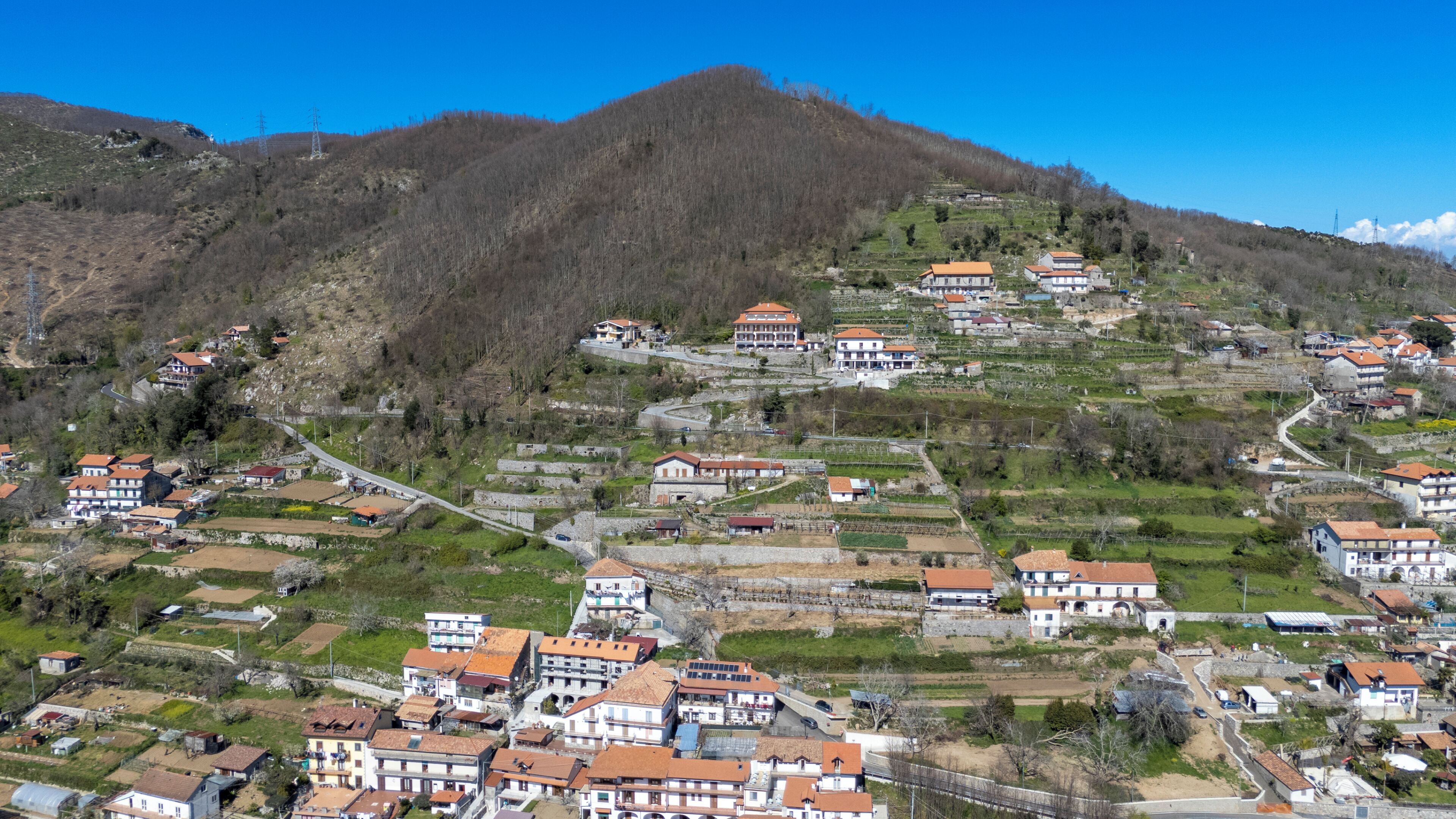 A hillside village with traditional buildings, terraced fields, and a prominent mountain in the background.