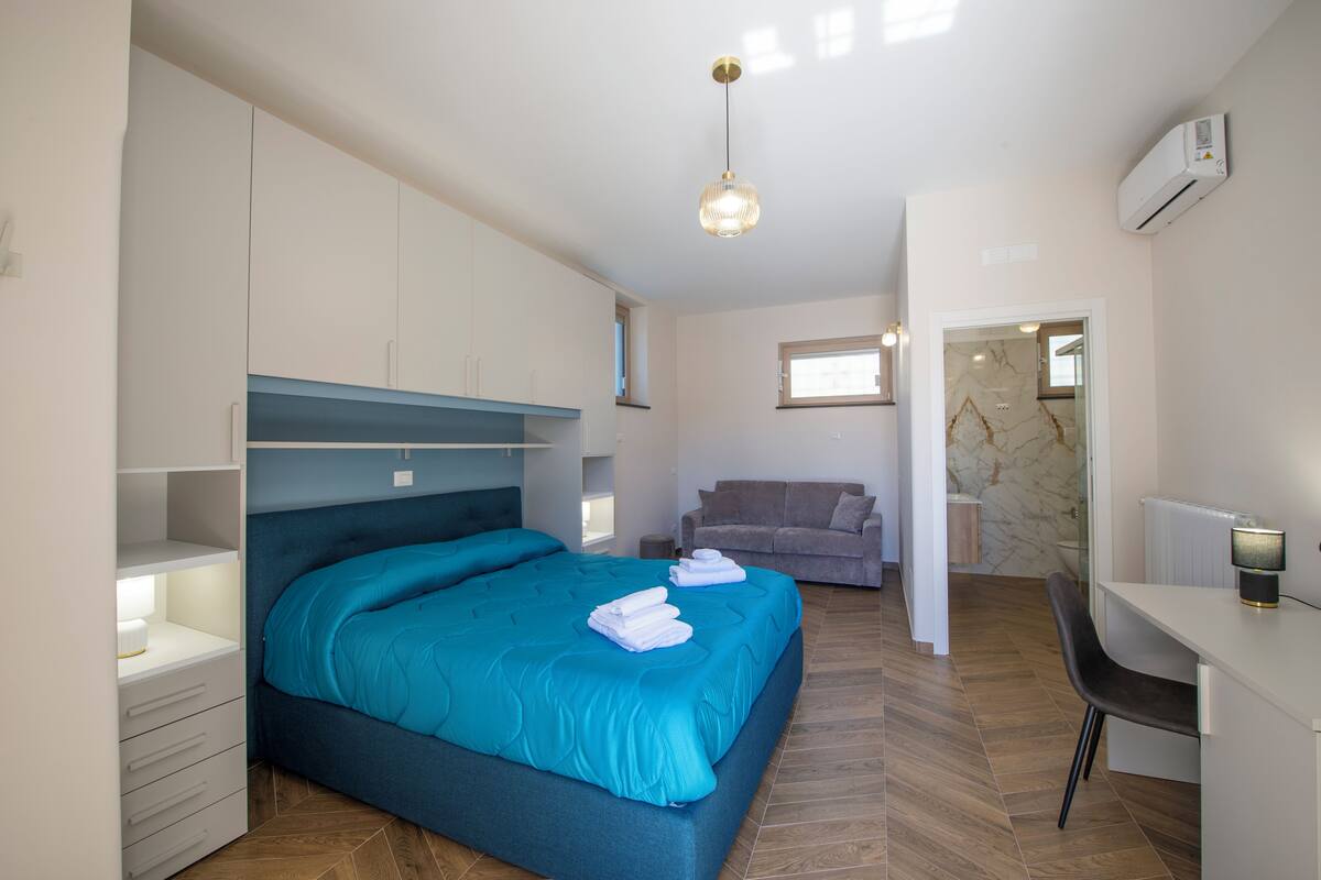 Quarto com cama, escrivaninha, cadeira e ar condicionado.