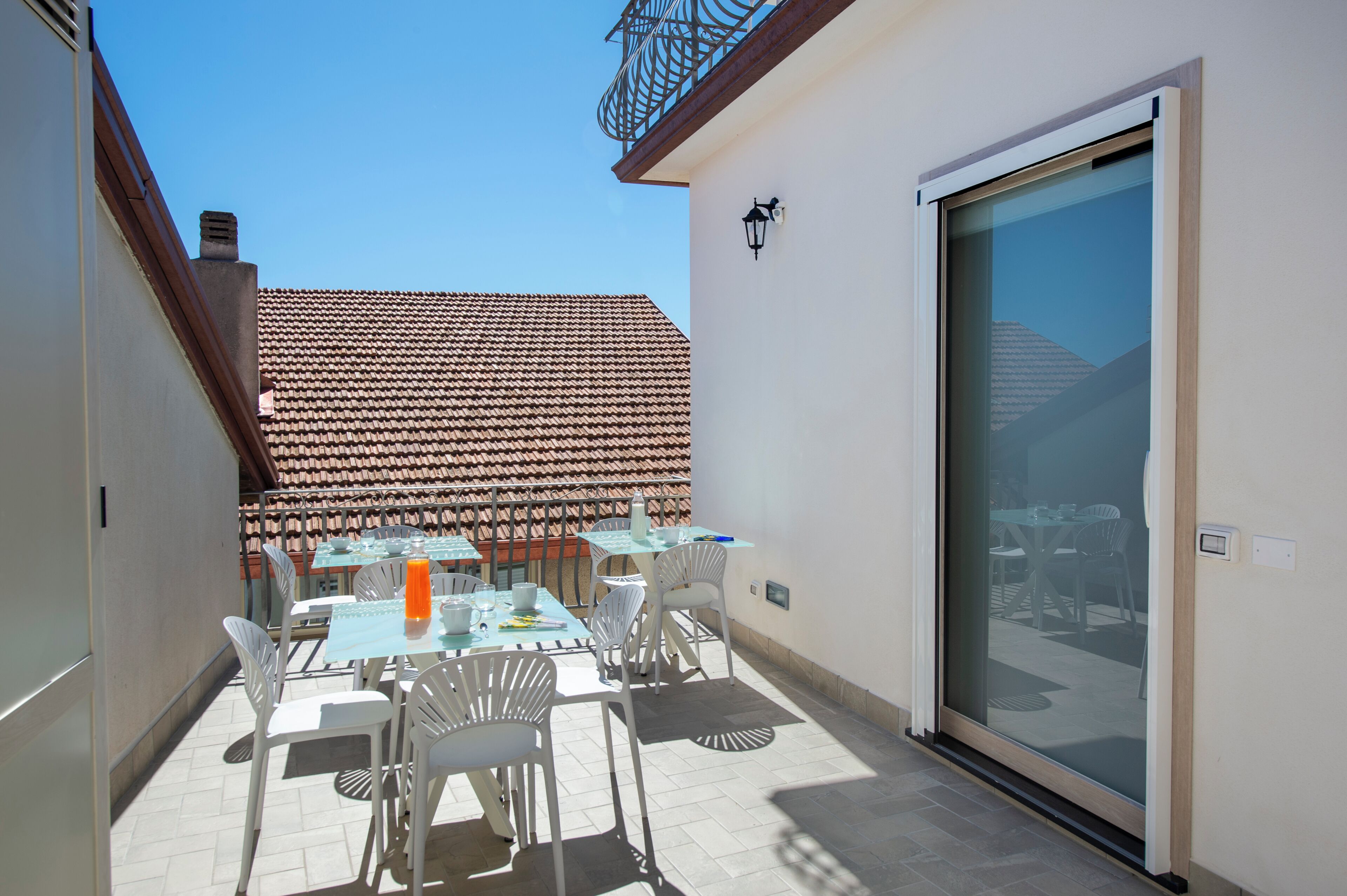 A patio with tables and chairs, a sliding glass door, and a tiled roof in the background.