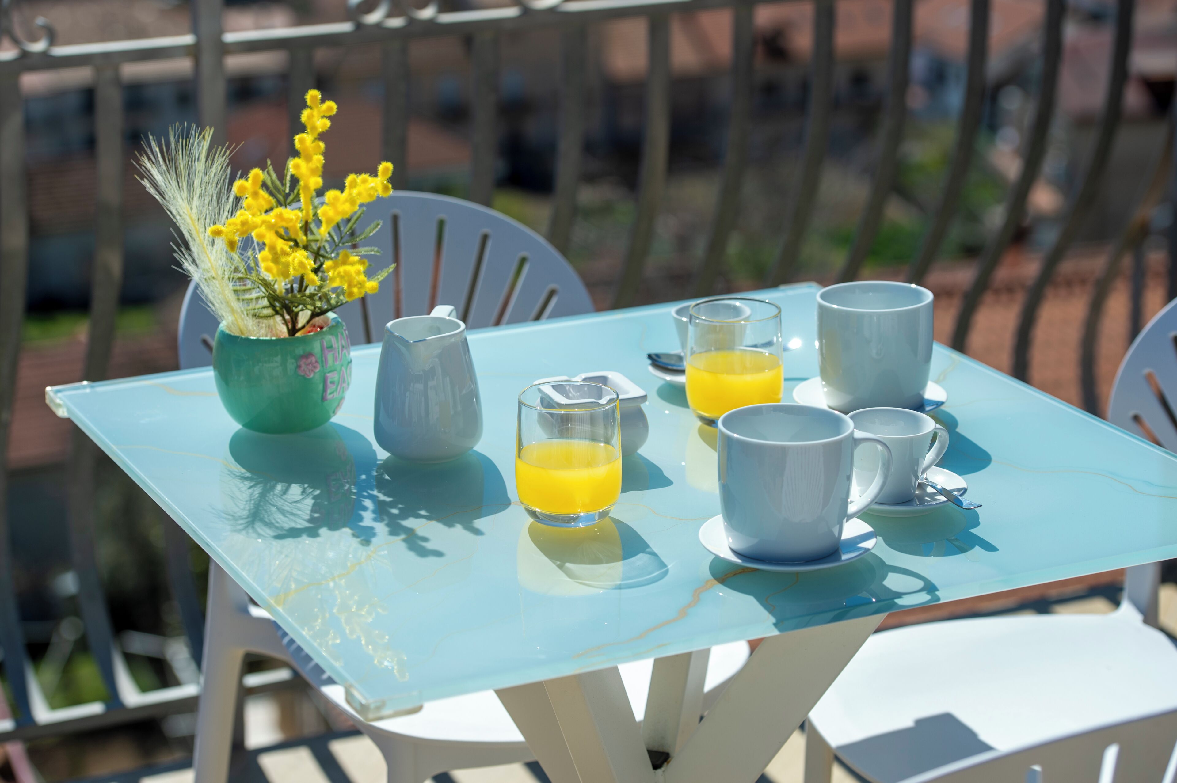 A table with a pitcher, glasses, and a cup, and a vase with yellow flowers.
