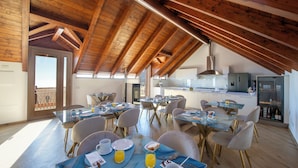 Un'ampia sala da pranzo con soffitti alti e travi in legno, una cucina con elettrodomestici moderni e un balcone con vista.
