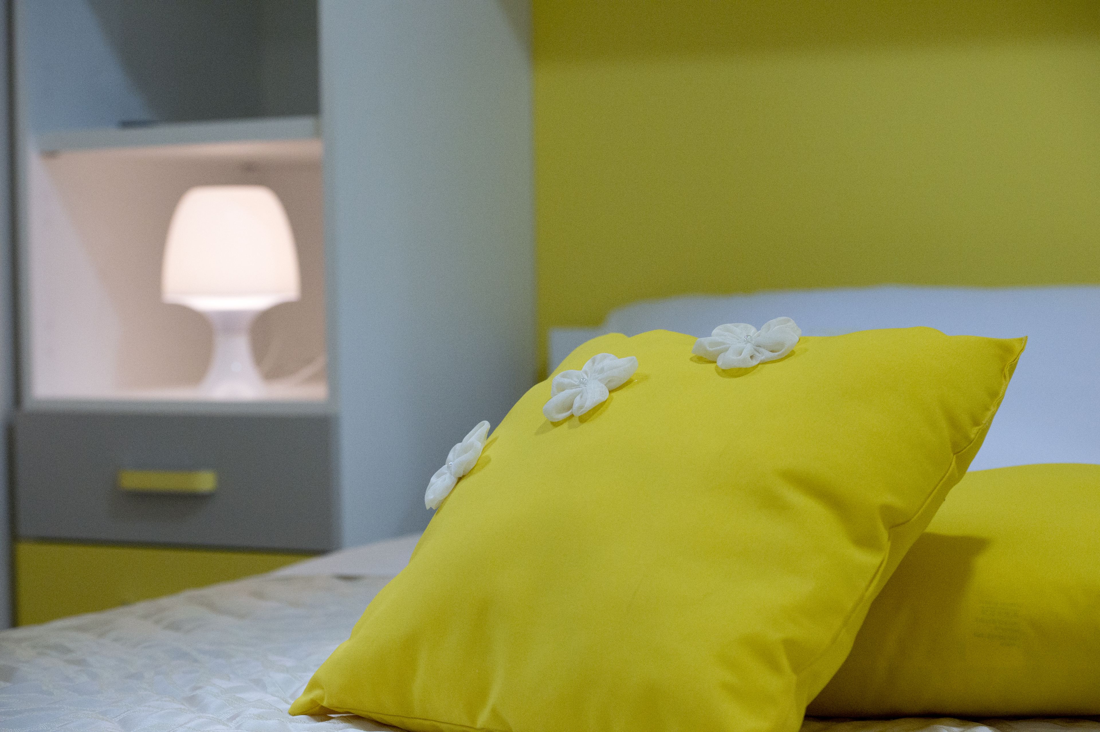 Una cama con almohadas amarillas y una lámpara blanca sobre una mesita de noche.