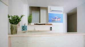 Une salle de bain avec un meuble-lavabo blanc, une plante en pot, une étagère en bois et un climatiseur fixé au mur.
