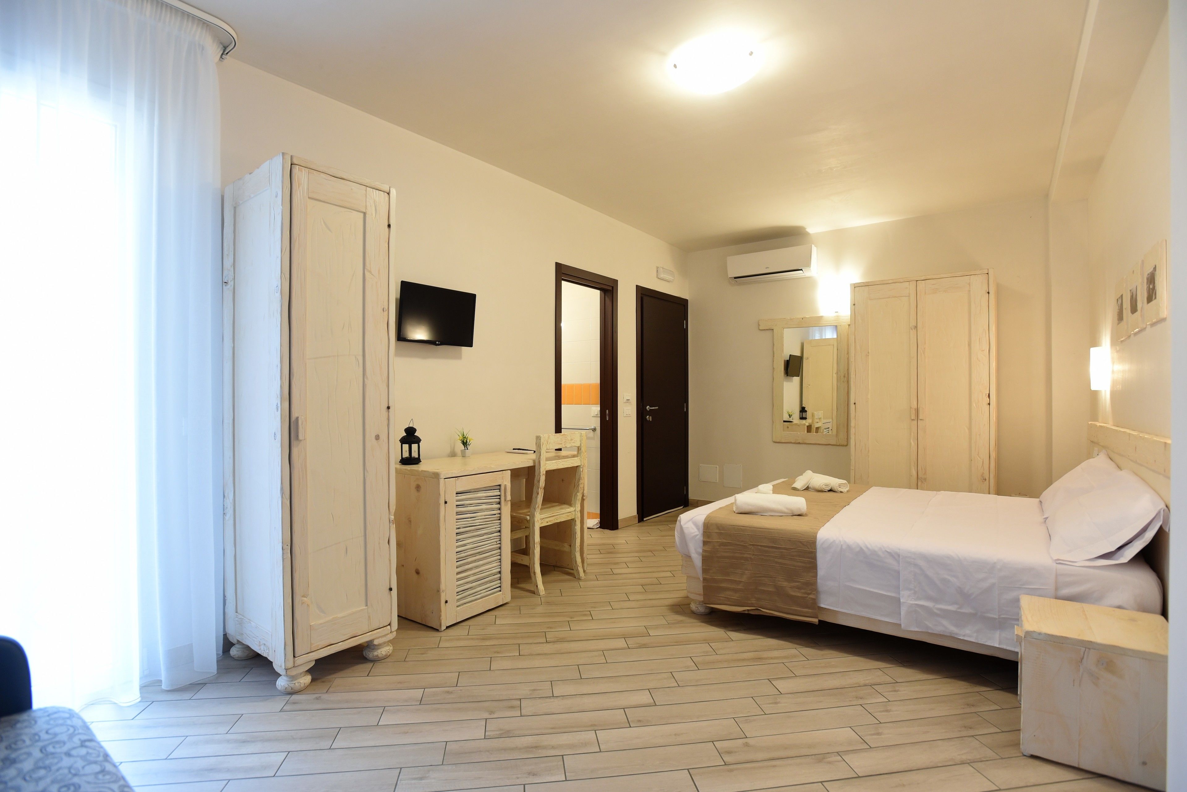 A hotel room with a bed, a desk, a chair, a wardrobe, and a television.