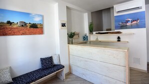 Une pièce comprenant un banc en bois, une petite table et une étagère fixée au mur, ornée d’objets décoratifs.