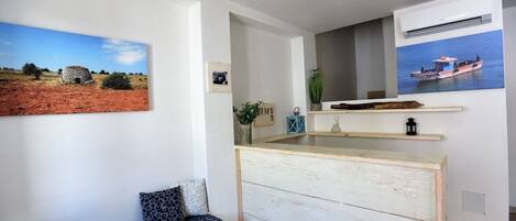 Una habitación con un banco de madera, una mesita y un estante de pared con adornos.