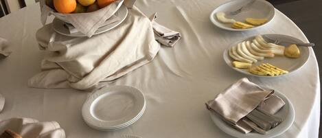 A table set with plates, cutlery, a bowl of fruit, and napkins.