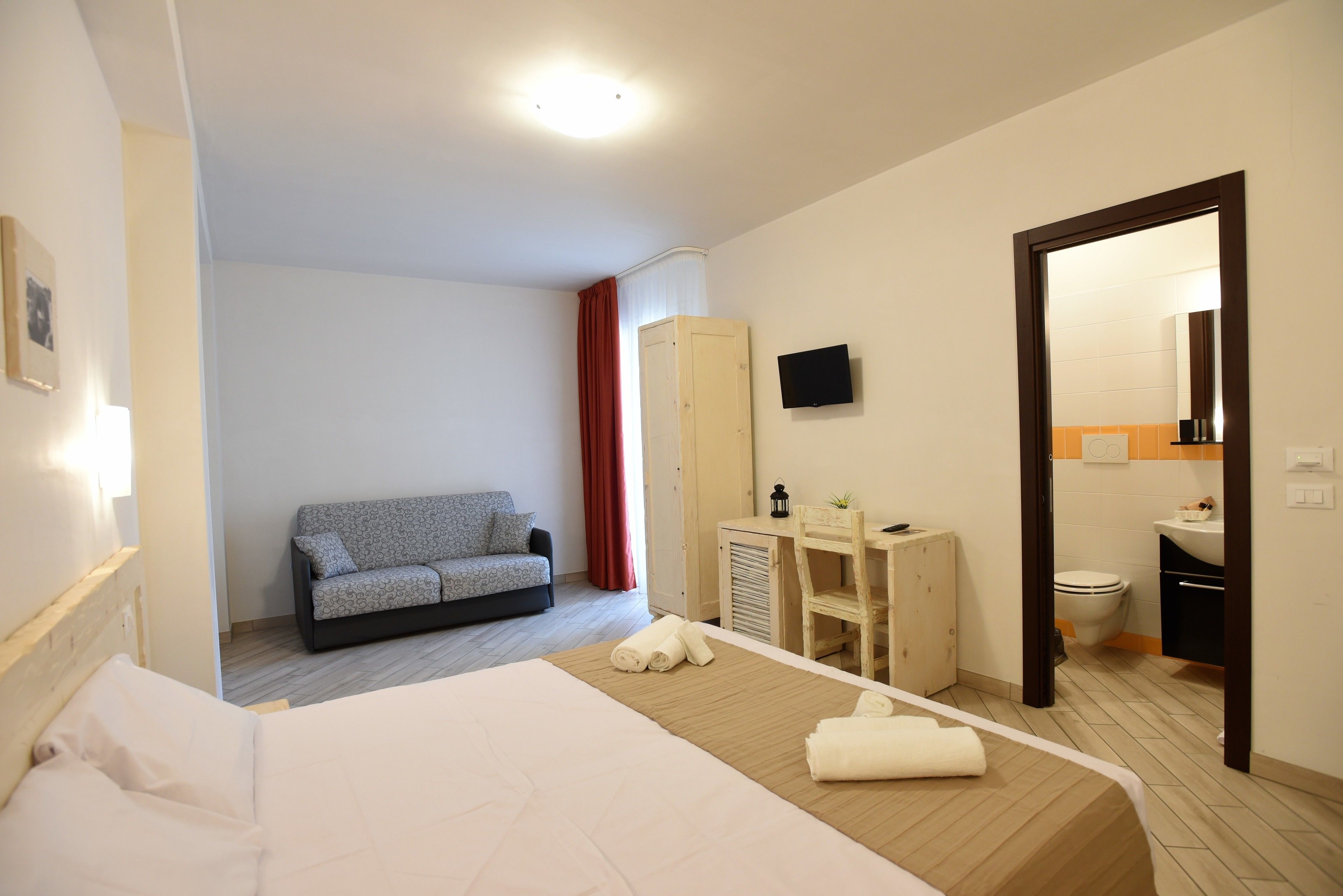 Quarto de hotel com cama, sofá, escrivaninha, espelho e banheiro.