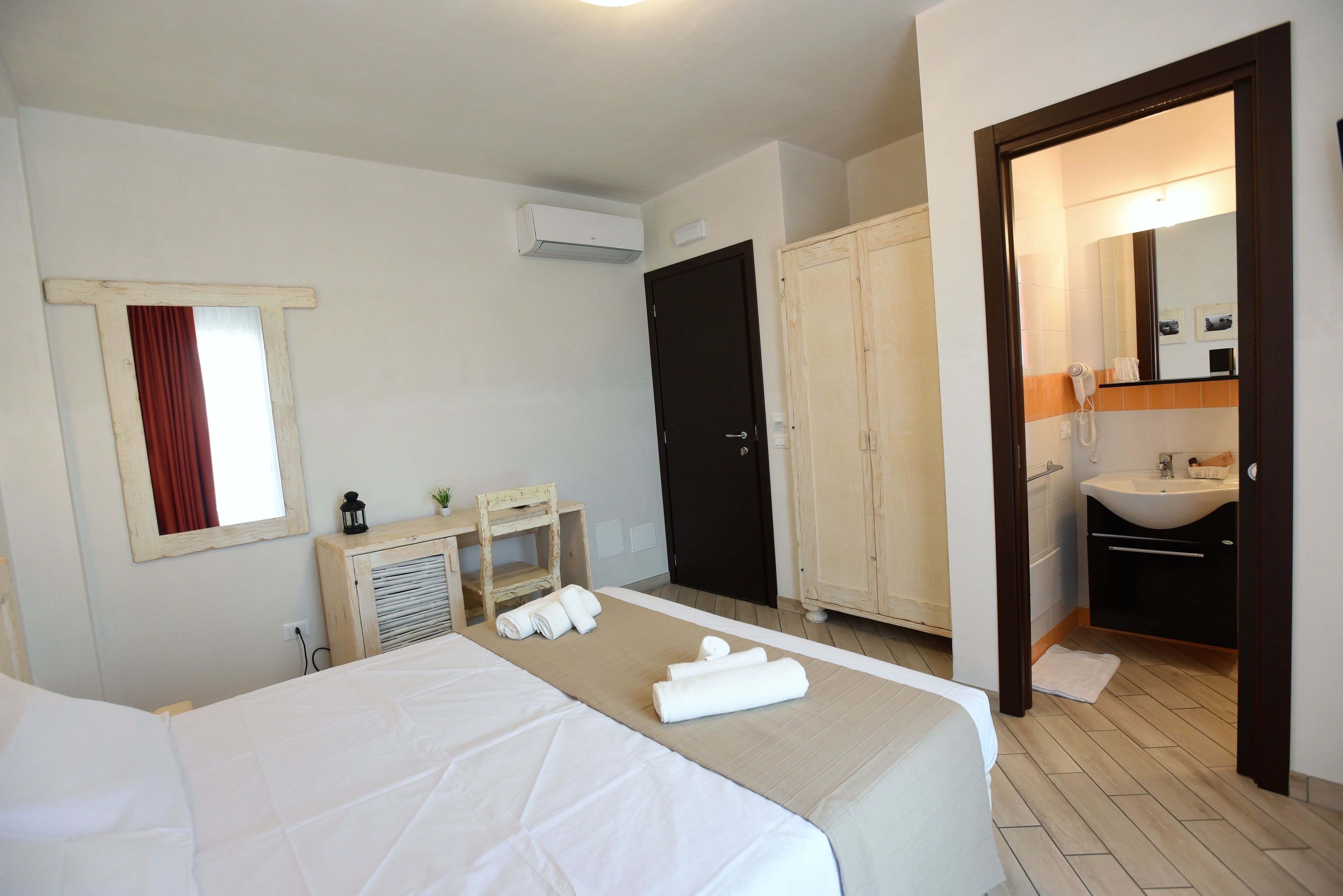 Een hotelkamer met twee bedden, een houten garderobe, een badkamer met wastafel en spiegel, en een airconditioner.