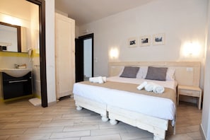 A bedroom with a wooden bed, a bedside table, a nightstand, a mirror, and a bathroom with a sink and towel rack. - Camere Le vie di Omero (Melendugno)