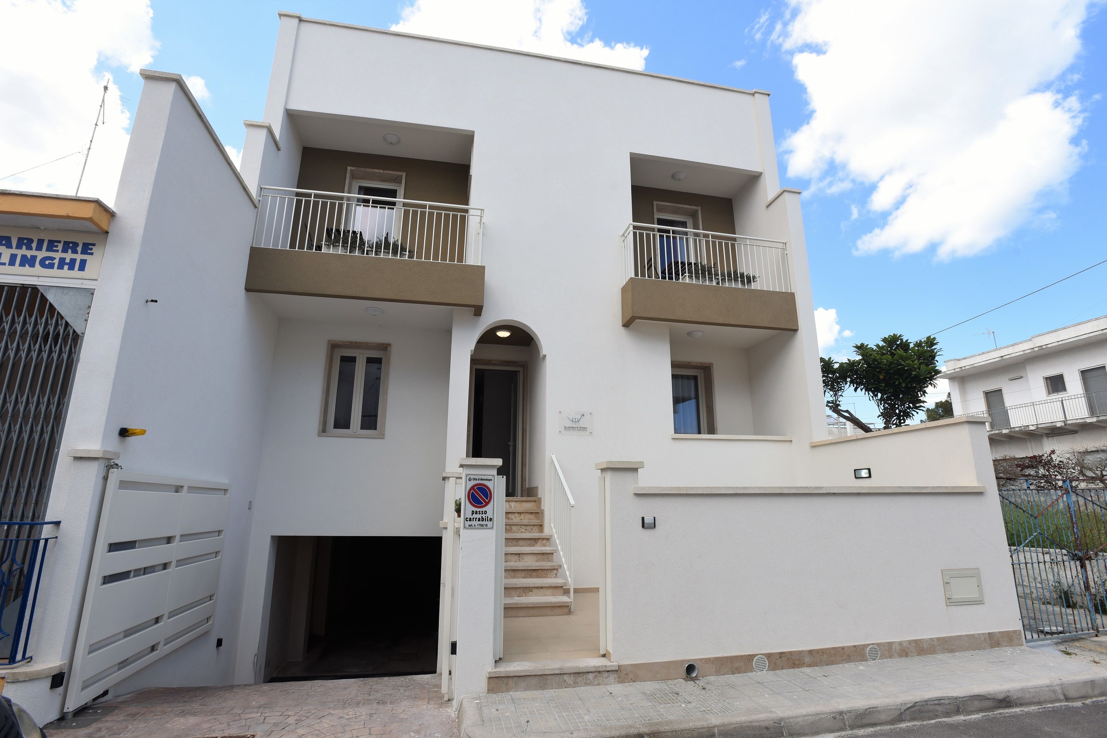 A two-story building with a white facade, a central entrance with a staircase, and balconies on each floor.