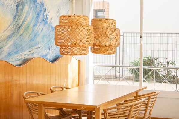 A wooden dining table with wicker chairs, a woven pendant light fixture, and a large abstract painting on the wall.