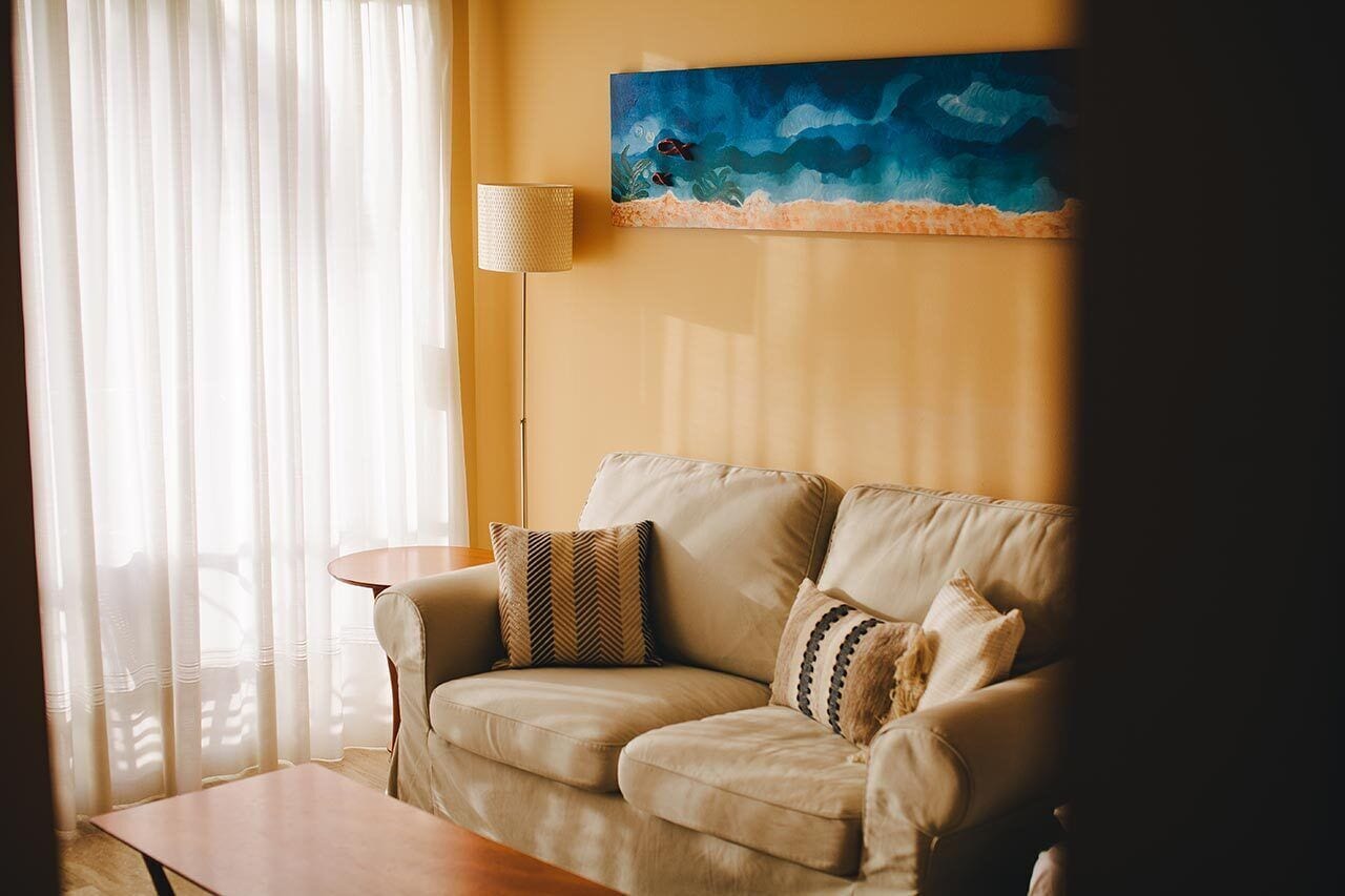 A living room with a beige sofa, a round coffee table, and a painting of a blue ocean scene on the wall.