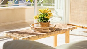 Een houten tafel met een gevlochten dienblad waarop een bloempot staat.