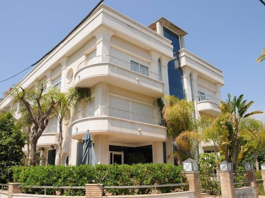 A multi-story building with a curved balcony, surrounded by lush greenery and palm trees.