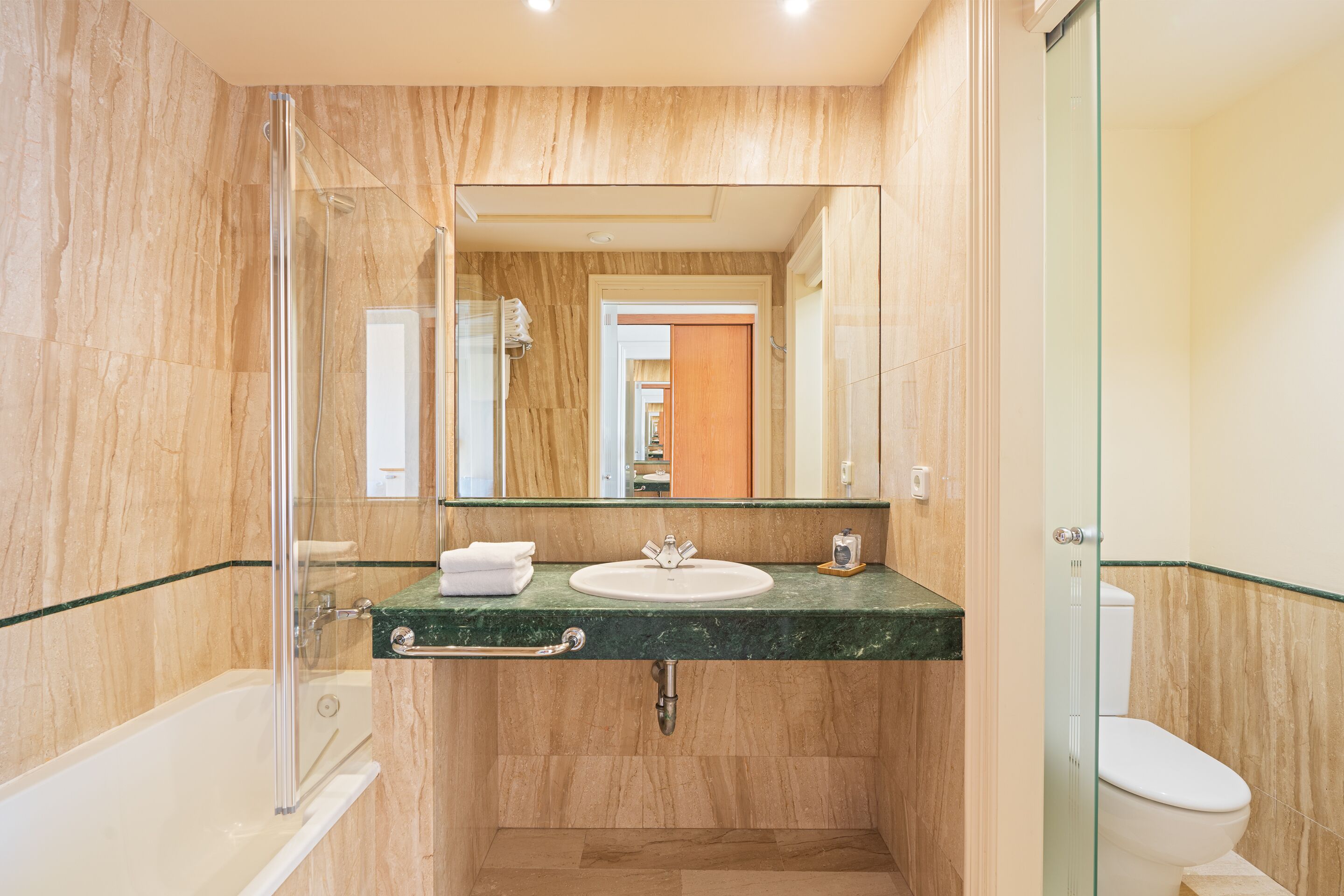 Une salle de bain avec une douche à parois de verre, un lavabo avec un plan de toilette en marbre et des toilettes.