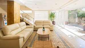 Een ruime woonkamer met een beige bank, een ronde salontafel en een grote potplant.