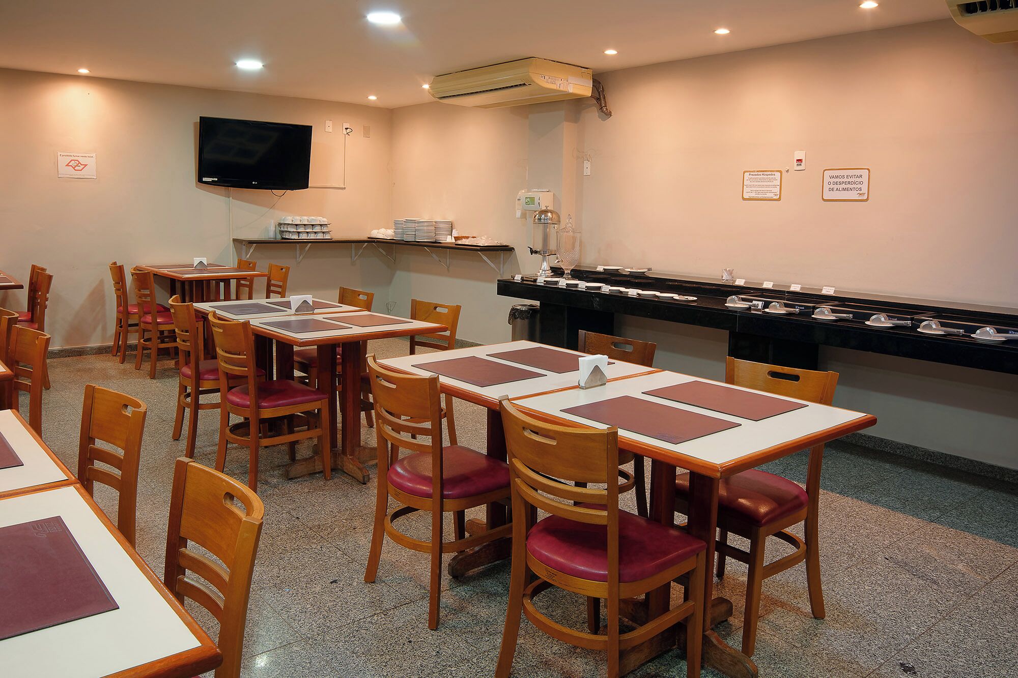 Un espace repas avec des tables et des chaises, un téléviseur fixé au mur et un buffet où sont présentés différents plats.