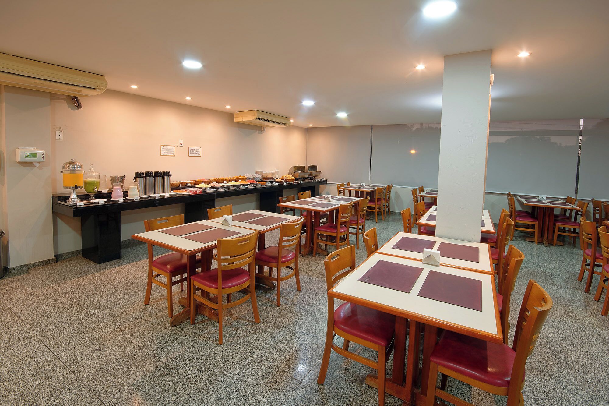 Un comedor con varias mesas y sillas, una barra de buffet con distintos alimentos, y un equipo de aire acondicionado en la pared.