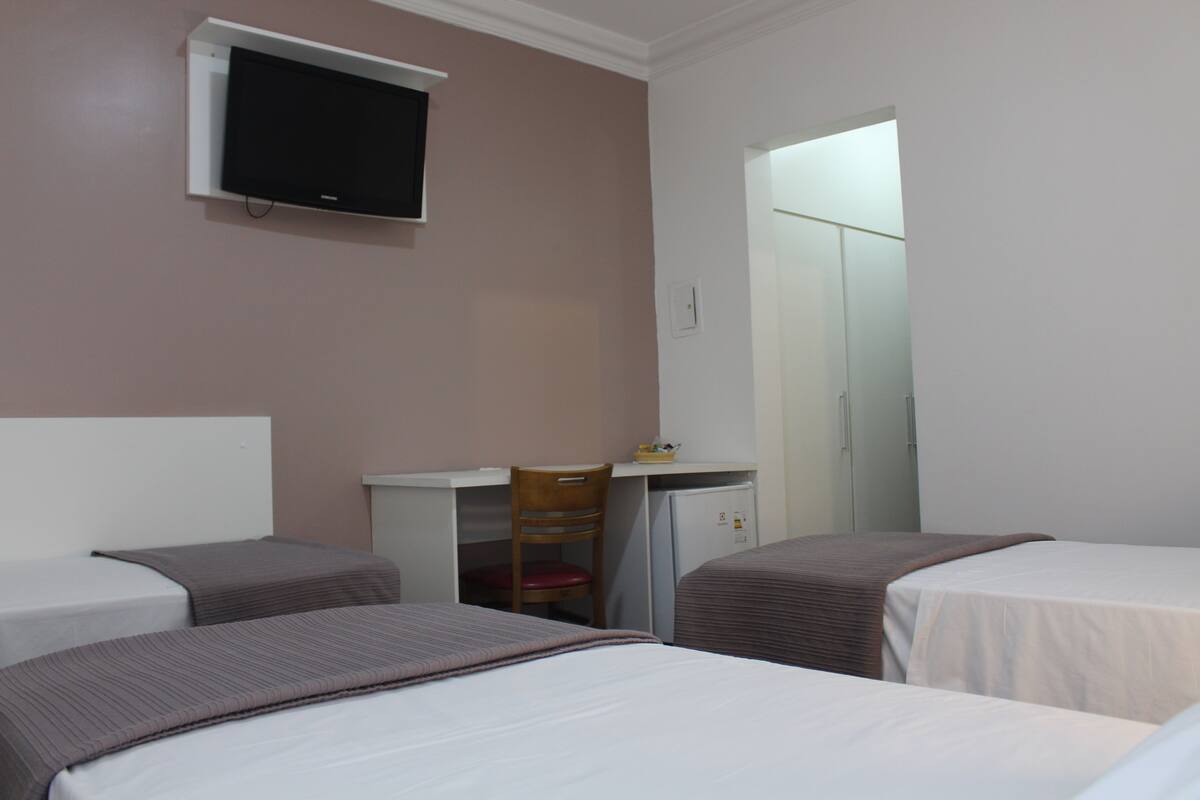 A hotel room with two beds, a desk, a chair, and a television.