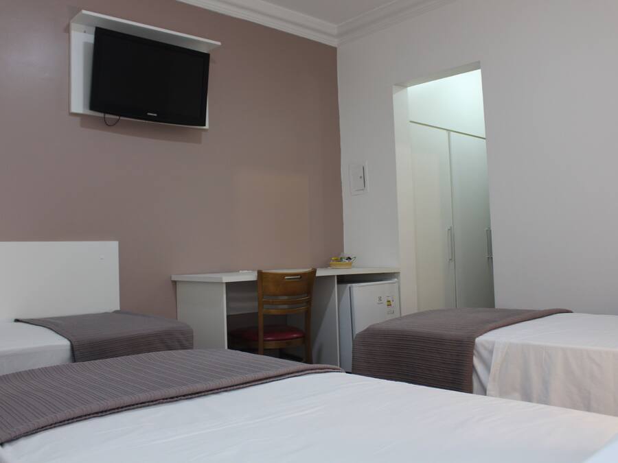 A hotel room with two beds, a desk, a chair, and a television.