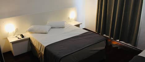 Una habitación de hotel con una cama, mesitas de noche y una cortina.