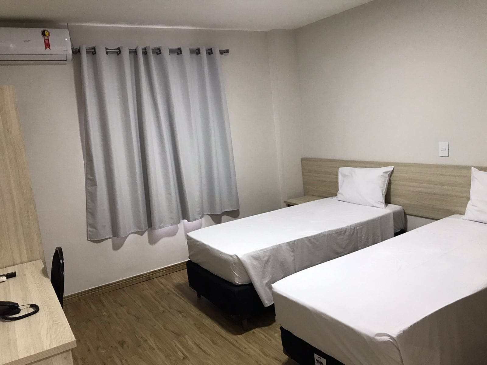 Una habitación de hotel con dos camas individuales, un escritorio con silla, una mesita y una cortina.
