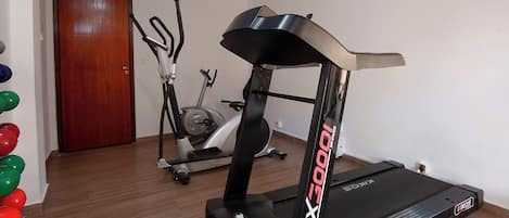 Uma academia com esteira, elíptico e bicicleta ergométrica.