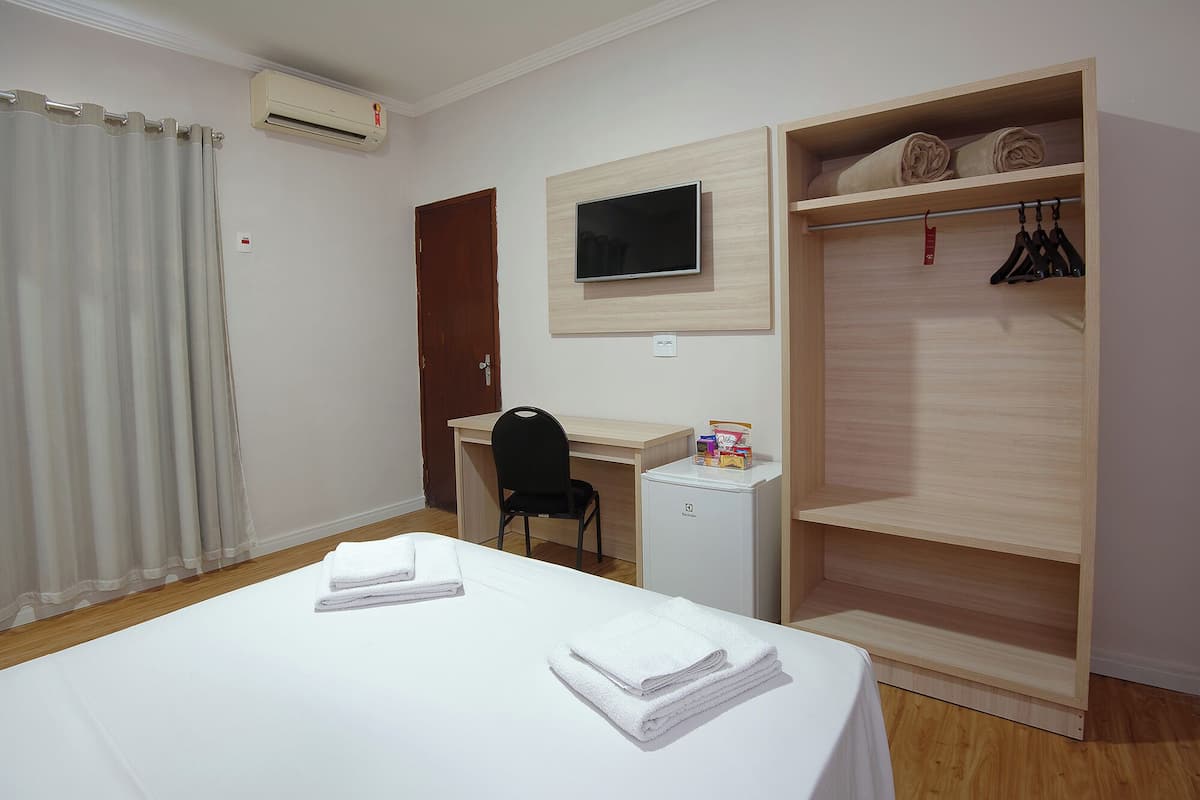 A hotel room with a bed, a desk, a chair, a TV, and a wardrobe.