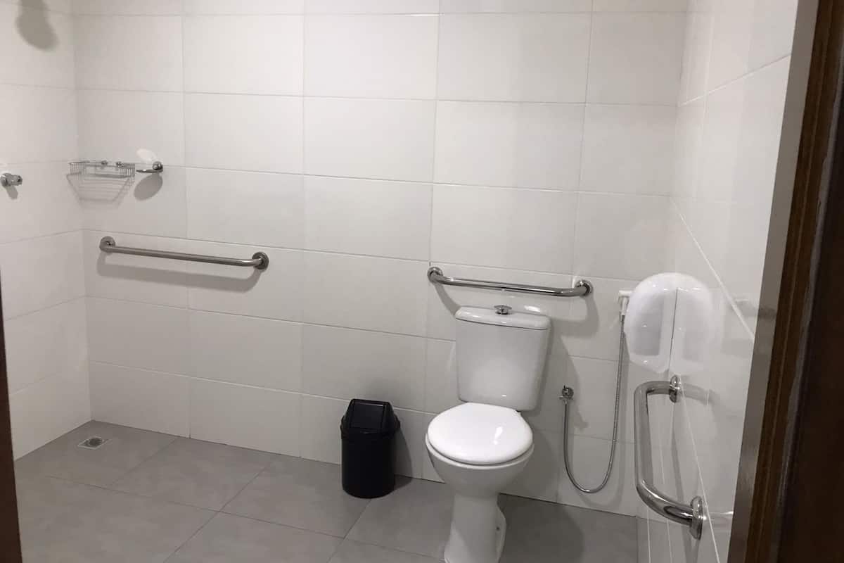 A modern bathroom with white tiles, a toilet, a bidet, a trash bin, and grab bars.