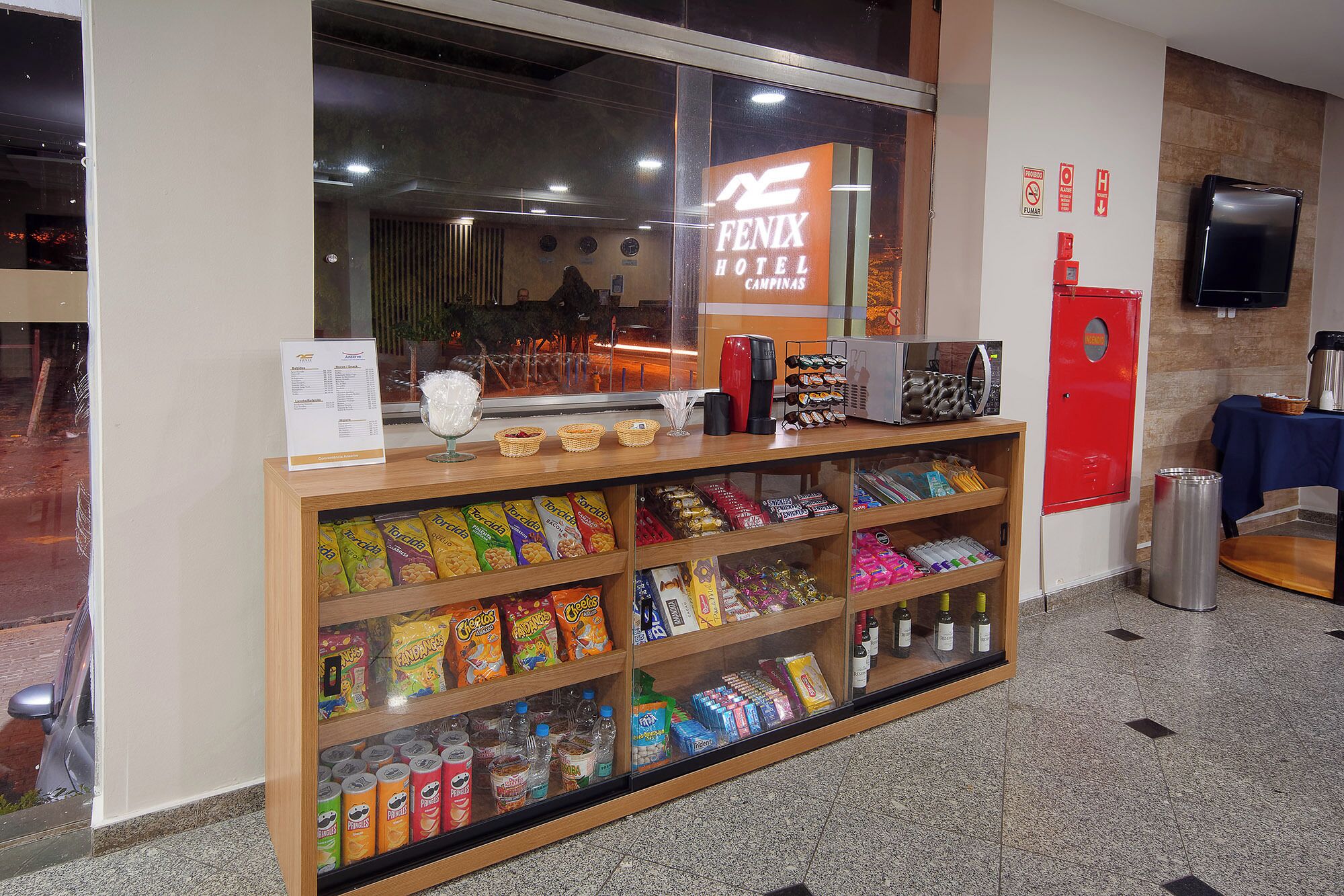 A hotel reception area with a display of snacks and beverages, a coffee machine, and a red fire extinguisher.